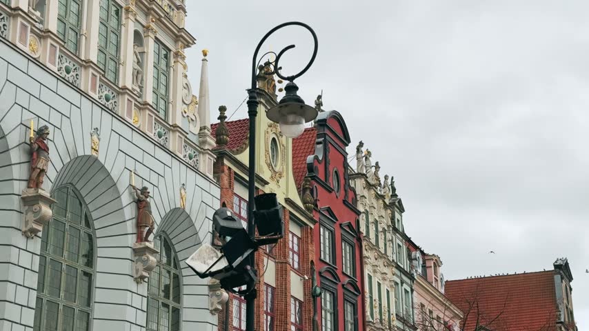 Historic row houses with ornate facades and a classic street lamp under an overcast sky in Gdansk, Poland. Authentic European architecture showcasing cultural heritage.