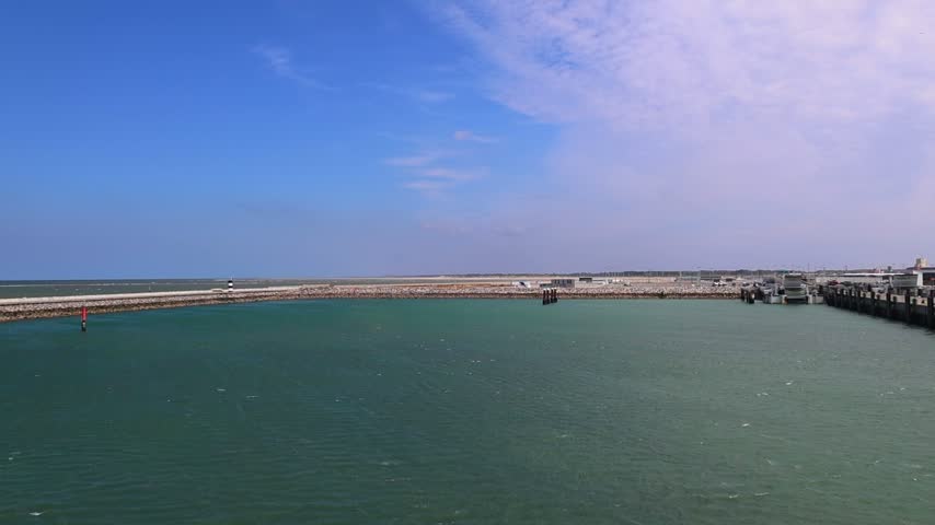 View across the turquoise waters of Calais ferry harbor toward the long breakwater and port entrance on the French coast.