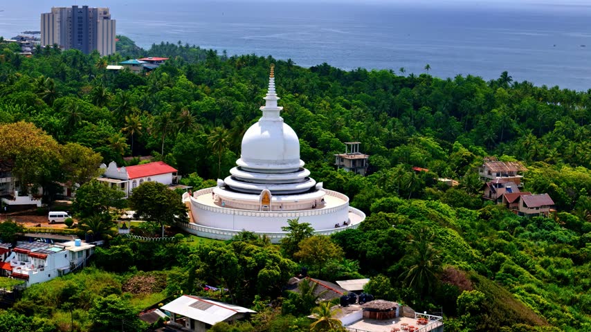 Aerial view of the white Japanese Peace Pagoda - Rumassala nestled among dense tropical trees overlooking the coastline in Unawatuna, Southern Province, Sri Lanka.
