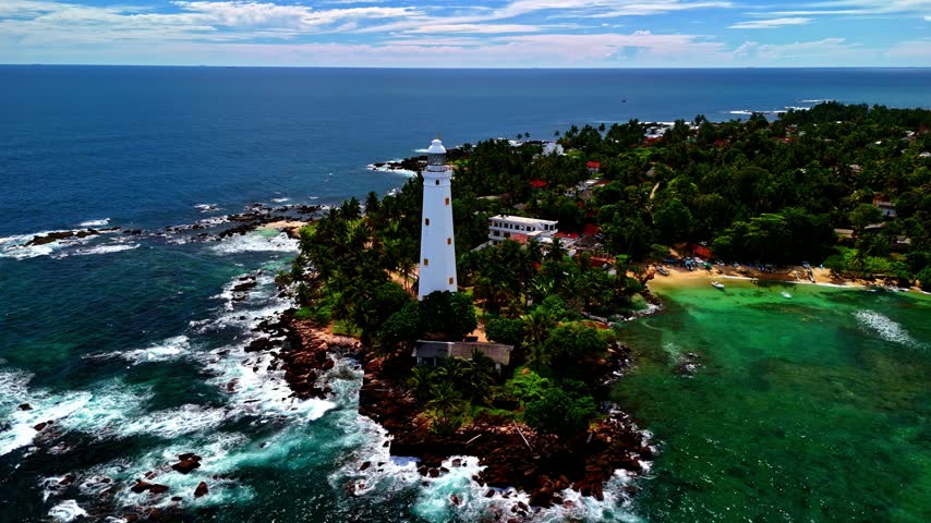 Aerial view of Dondra Lighthouse surrounded by lush tropical trees and rocky coastline with turquoise waters in Dondra, Southern Province, Sri Lanka.