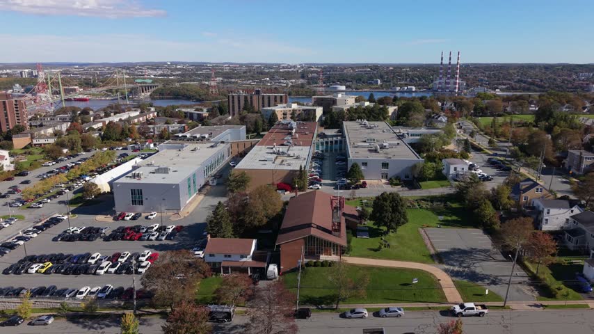 A steady aerial view surveys the Institute of Technology buildings, parking lots, and surrounding city in Halifax, Nova Scotia, Canada, beneath a bright autumn sky.