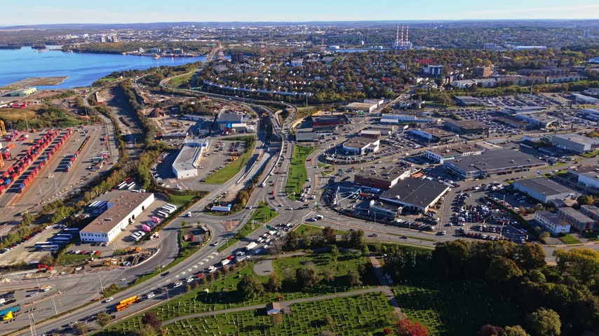 An aerial view of vehicles moving through a broad highway interchange in Halifax, Nova Scotia, Canada, with city buildings, roads, and waterfront stretching into the distance.