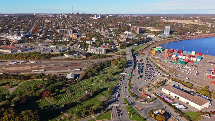 Cars stream through a broad highway interchange beside Halifax Harbour and the colorful port in Halifax, Nova Scotia, Canada, under clear daylight.