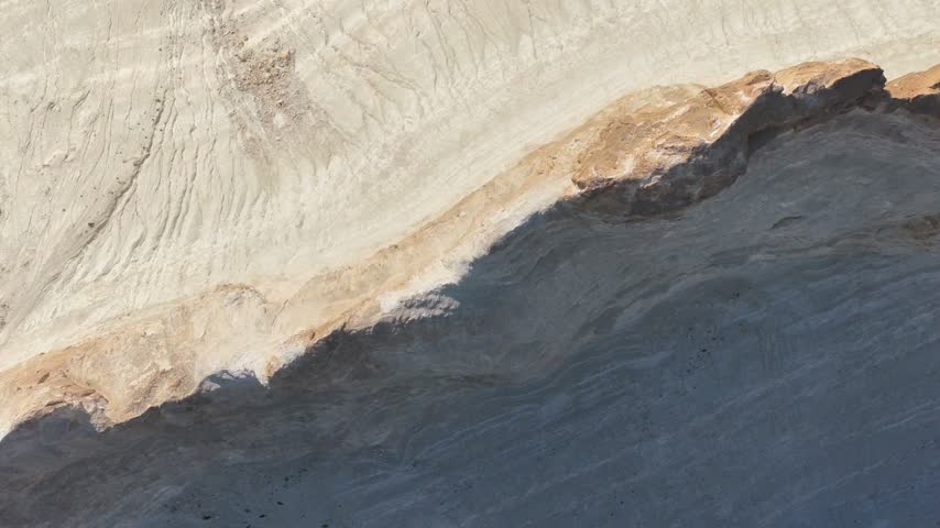 A top-down aerial follows the curving crest where sunlit white chalk meets a broad blue-gray shadow, turning Bozzhyra