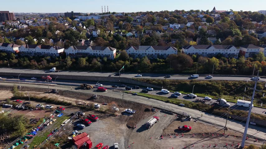 Traffic moves along a sweeping highway interchange above a city neighborhood in Halifax, Nova Scotia, Canada, beneath clear daylight skies.