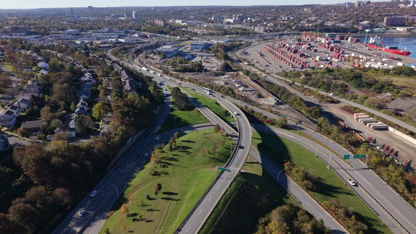 Cars travel along curving highway ramps and adjoining roads in Halifax, Canada, with neighborhoods, trees, and green space stretching across the landscape in daylight.