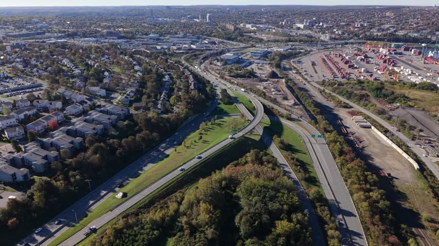 An elevated daytime view follows traffic along a Halifax highway interchange, with curving roads, green space, and nearby neighborhoods stretching across Nova Scotia.