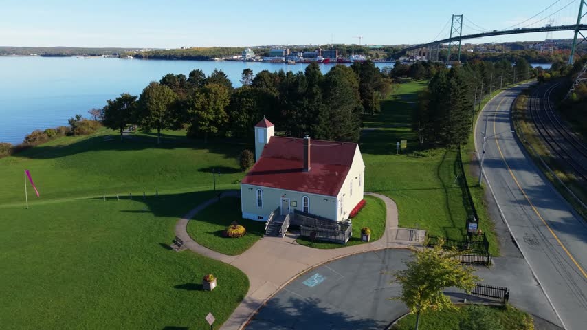An aerial view circles Africville Museum in Halifax, Nova Scotia, set among green parkland near the water and bridge, honoring the history and loss of an African Nova Scotian community.