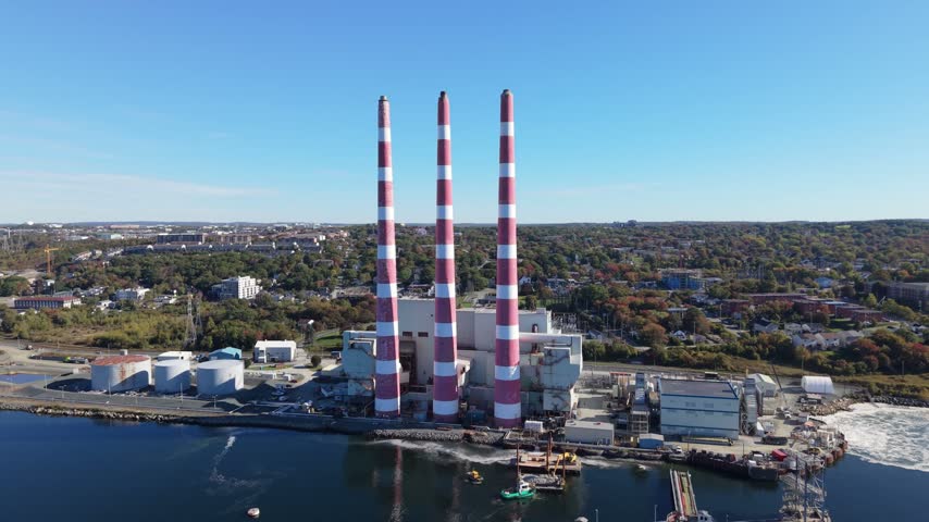 Three red-and-white power station stacks rise over the waterfront in Halifax, Nova Scotia, Canada, as an aerial view reveals the surrounding city on a clear day.