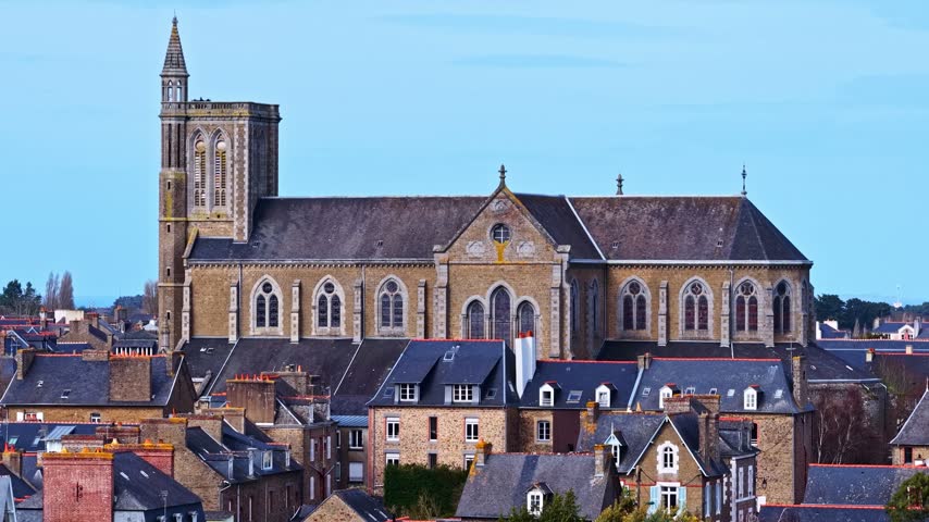 Aerial view of a historic stone church with a tall bell tower surrounded by traditional rooftops in France.