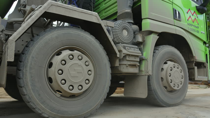 Massive green construction vehicle demonstrates large tires and heavy chassis. Outdoor working area reflects active industrial scene