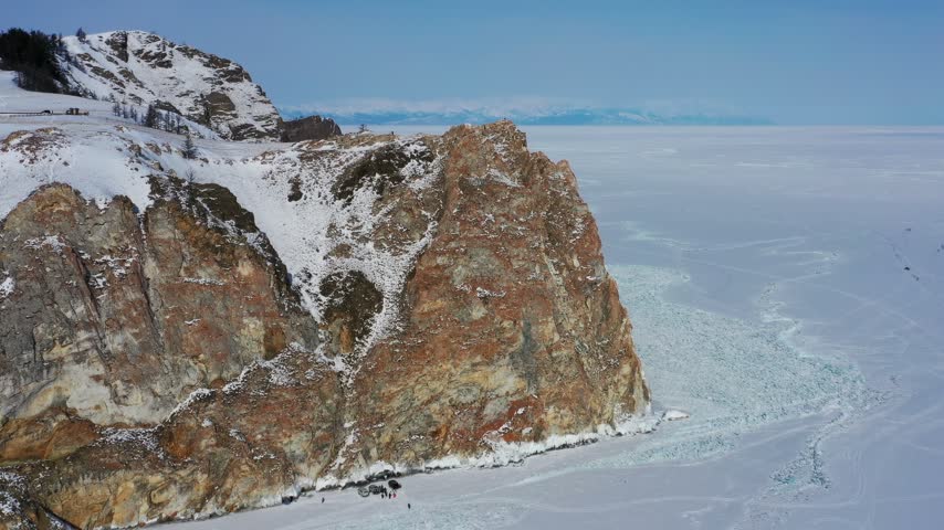 Aerial view of Lake Baikal featuring snow-covered rocky cliffs and frozen ice surface in Russia.