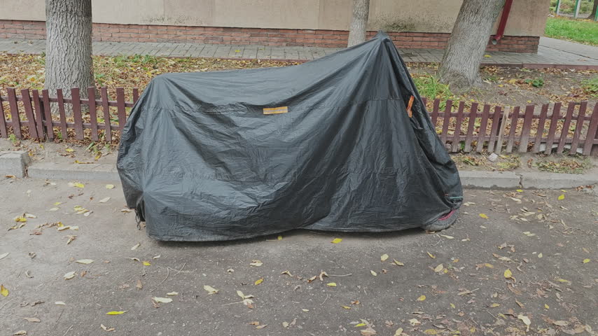Motorcycle protected by a waterproof cover parked on a city street during a windy autumn day