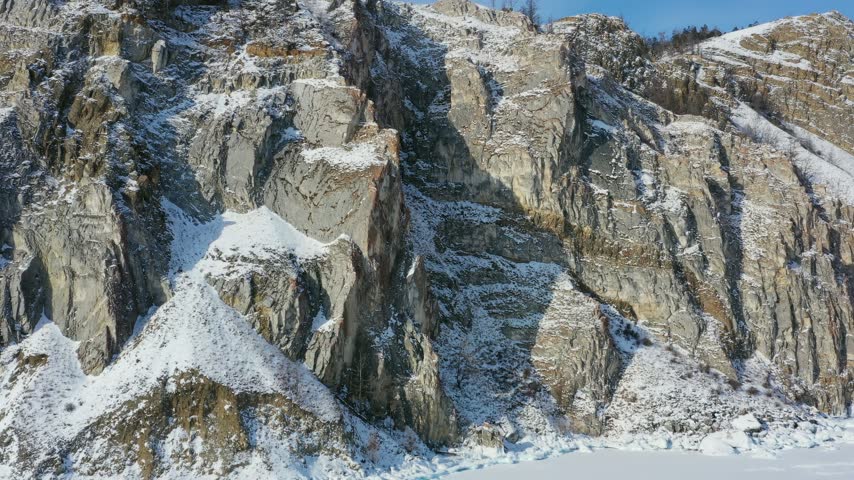 Aerial view of snow-covered rocky cliffs along the frozen shoreline of Lake Baikal in Russia.