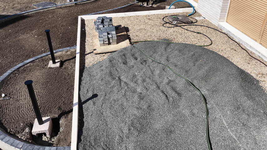 An elevated view moves closer to a kneeling landscaper working on soil between a curved border and a house.