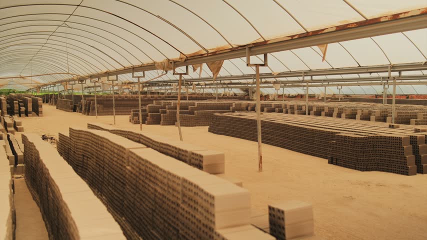 A worker pushes a loaded handcart between rows of freshly formed clay bricks drying beneath a translucent arched roof at a brick factory in Mang Thit, Vietnam.