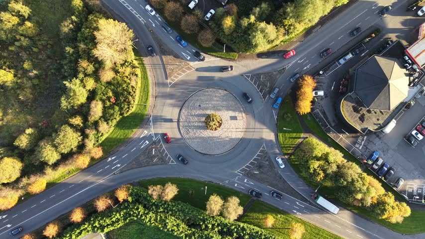Top down drone view of a busy roundabout with moving vehicles, landscaped green spaces and autumn trees in Castlebar, County Mayo, Ireland.