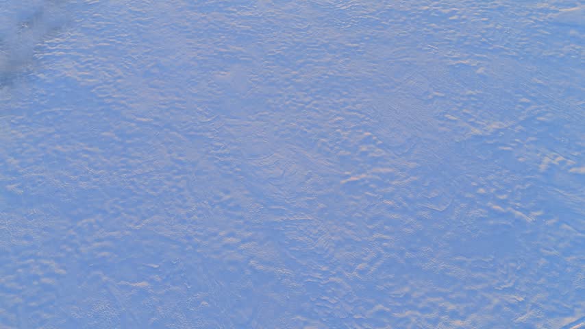 Snow lies on the ground. Flight over the field in winter at sunset time. Lapland, Finland.