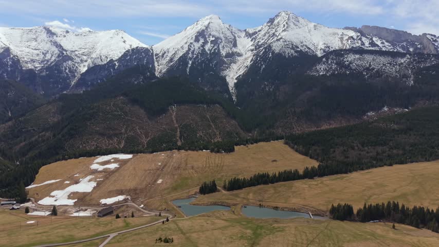 Majestic snow covered peaks of the High Tatras mountains in Slovakia. A stunning alpine landscape featuring a green valley, forest, and small lakes