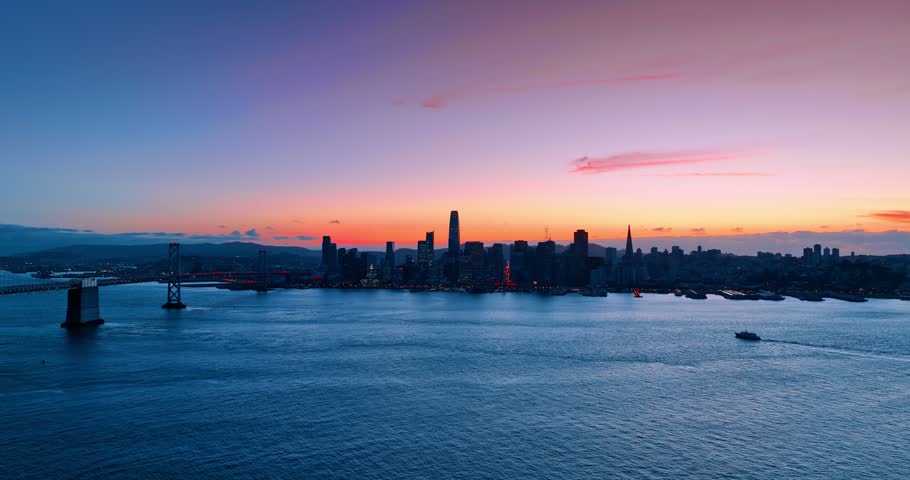Dark skyline of downtown San Francisco, California, USA against colorful sky. Drone footage over the waterscape of the bay at sunset.