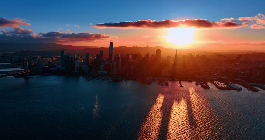 Approaching San Francisco skyline in the light of setting sun. Drone footage over the bay waterscape at sunset.