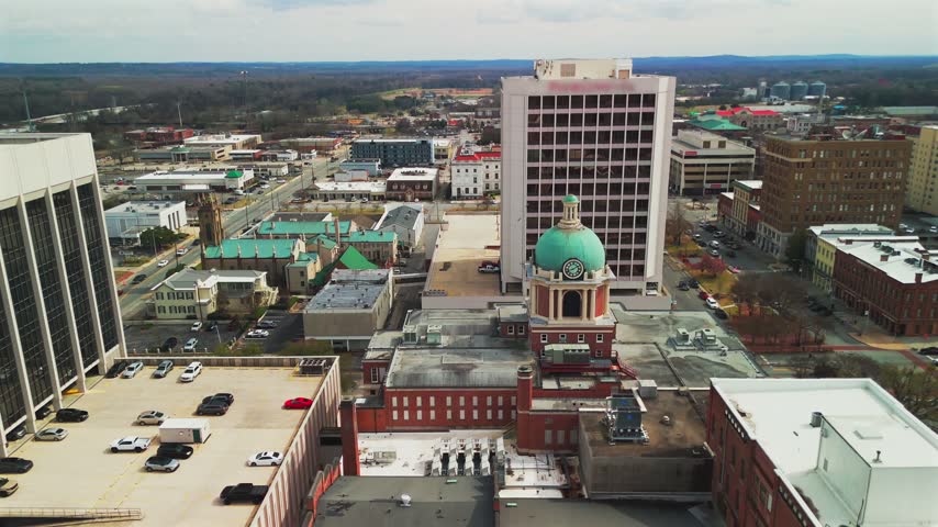 Drone view of a green-domed clock tower framed by office buildings, historic rooftops and downtown streets in Macon, Georgia