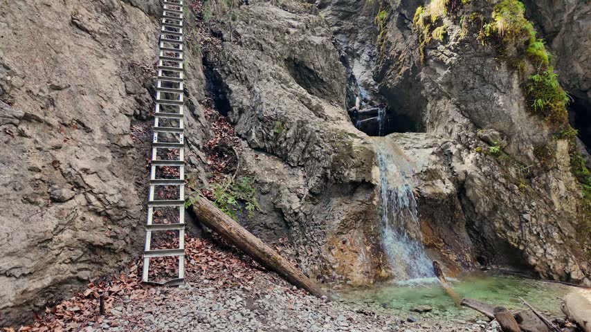 Moving shot looking up a steep gorge with a hiking ladder and a small waterfall. This trail is located in the Sucha Bela canyon, Slovakia