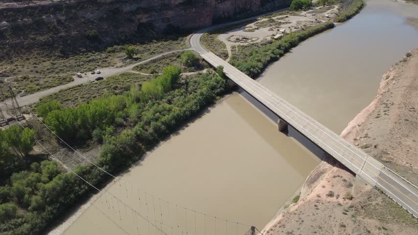 Aerial view of bridge spanning winding river in red rock desert.