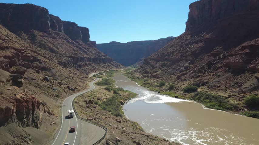 Aerial view of scenic road beside river between tall canyon cliffs.