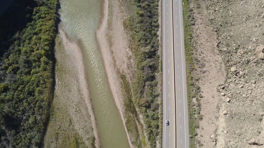 Top down aerial view of vehicles on road beside riverbank.