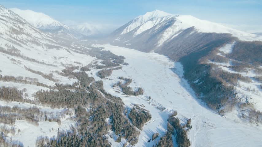 Aerial View of Snow Covered Mountain Valley with Frozen River and Pine Forest