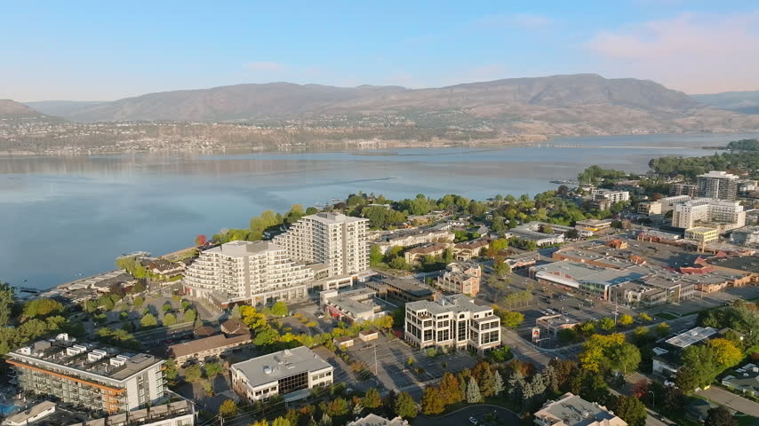 Non-descript town next to a body of water, during daytime, showing some taller and shorter buildings and a main stretch of road with cars driving by. On a quiet, sunny day.
