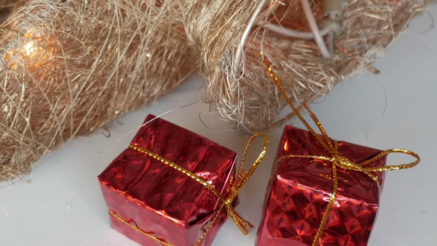 Christmas decorations on white table. Red bauble, red small gift box, toy drum and decorative light tree with lights with lights made out of fibers on white table next to other festive decorations.
