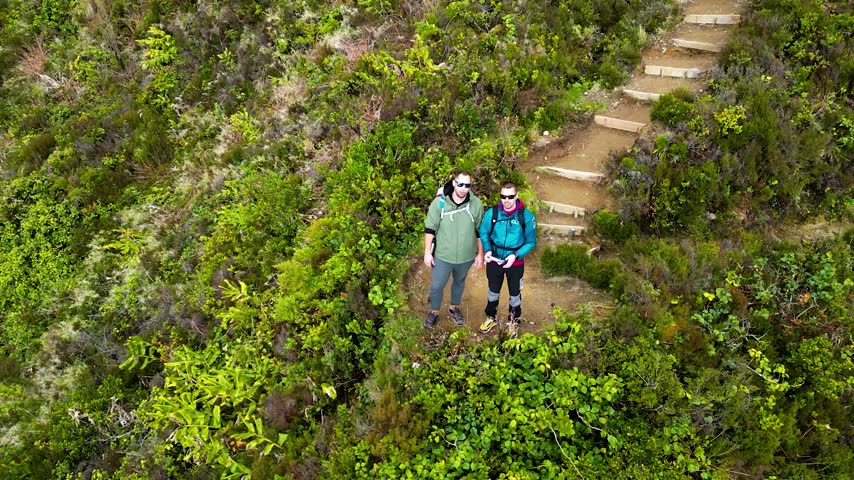Hikers walk along a winding trail with stone steps beside a lush green lake hillside