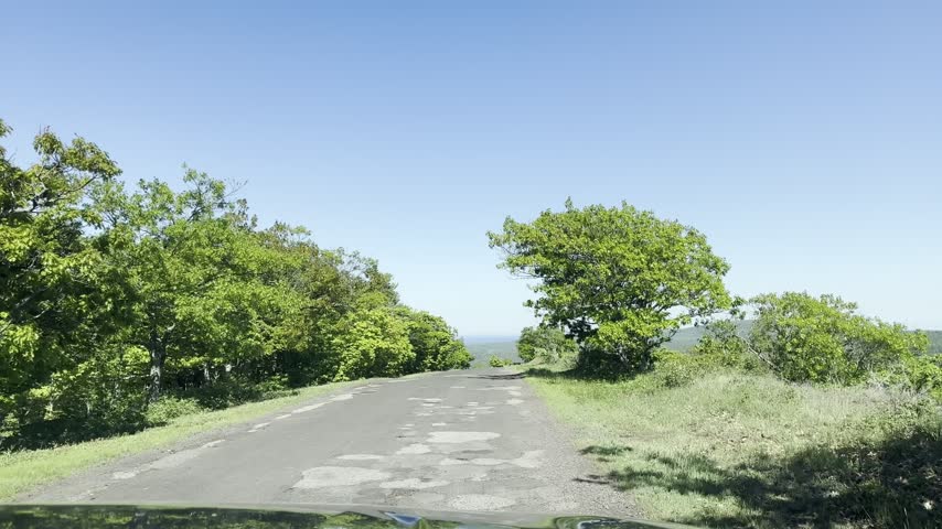 A forward moving view descends Brockway Mountain Drive near Copper Harbor Michigan past leafy trees and low stone walls with blue lakes and forested hills beyond.