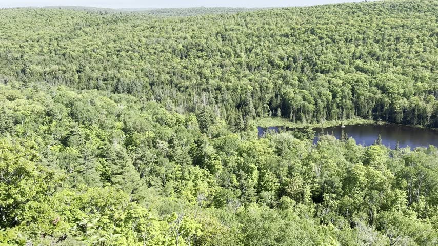 Elevated view sweeps across green woodland and a small pond at Brockway Mountain Overlook in Michigan with forested hills extending toward the horizon.