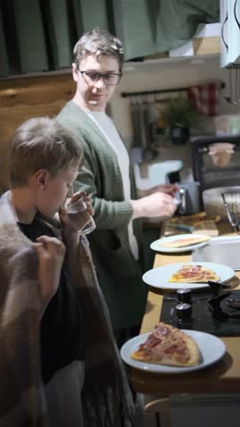 Father and son preparing pizza in kitchen together, smiling, enjoying cozy domestic moment.