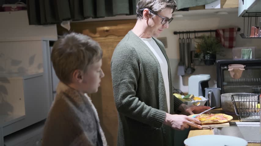 Father and son preparing pizza in kitchen together, smiling, enjoying cozy domestic moment.