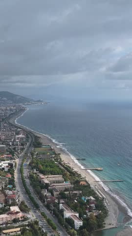 Elevated view of a densely built coastline, beach, ocean, and highway beneath overcast clouds.