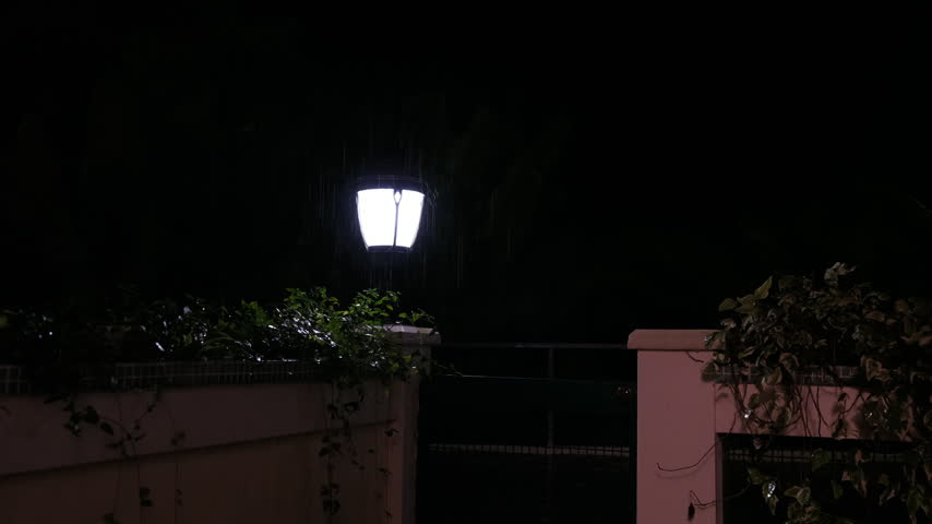 Static shot of a garden lamp brightly illuminating dark falling raindrops on a wet outdoor ledge with sound in Tsikhisdziri Georgia.
