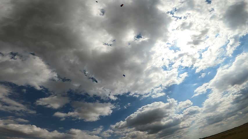 Skydivers with wing-type parachutes fly through a beautiful, cloudy sky