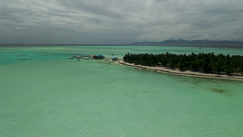 Cinematic aerial view of Onok Island in southern Palawan, Philippines, revealing a pristine white sandy shoreline, shallow mint-green waters, intricate coral reef patterns and a secluded tropical island surrounded by the Sulu Sea.