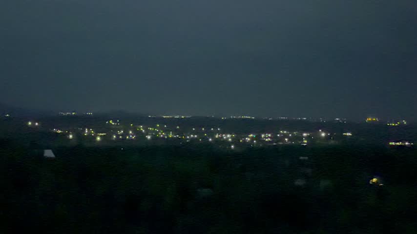 A view of a small mountain town at twilight. Bright lights from houses set against the backdrop of mountains at twilight.
