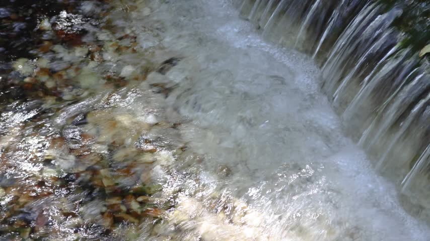 Small waterfall cascade flowing smoothly over rock into clear stream
