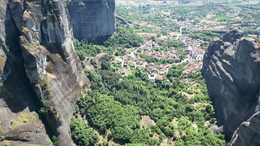 Aerial view of Kastraki village nestled between giant monolithic rock pillars and green valley at foot of Meteora cliffs in Thessaly Greece.