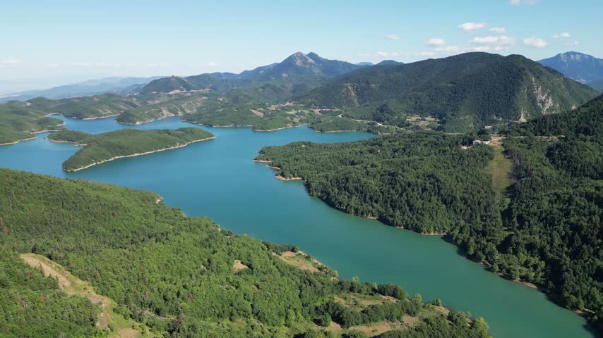Aerial high angle view of Lake Plastira turquoise water surrounded by dense pine forest hills and Pindus mountain peaks in Thessaly region Greece.