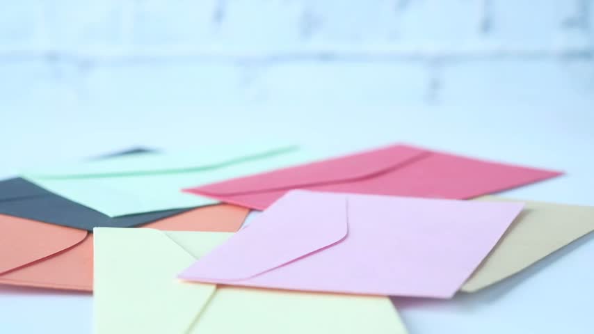 Person placing single red rose on pile of colorful envelopes. Romantic greeting concept with vibrant stationery on white wooden surface. High quality footage for love and celebration.