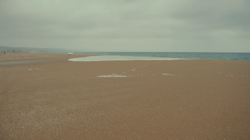 A wide sandy Newport Beach shoreline shows signs of rising tides and coastal storm conditions.