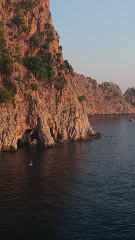 Rocky coastal cliffs rise above dark calm water with a small boat offshore.