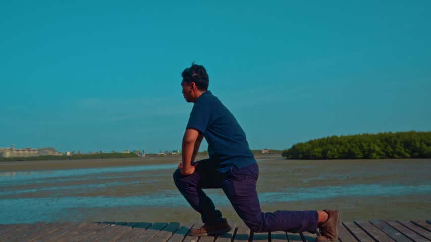 Young man stretching legs outside on wooden pier in scenic coastal environment during calm day